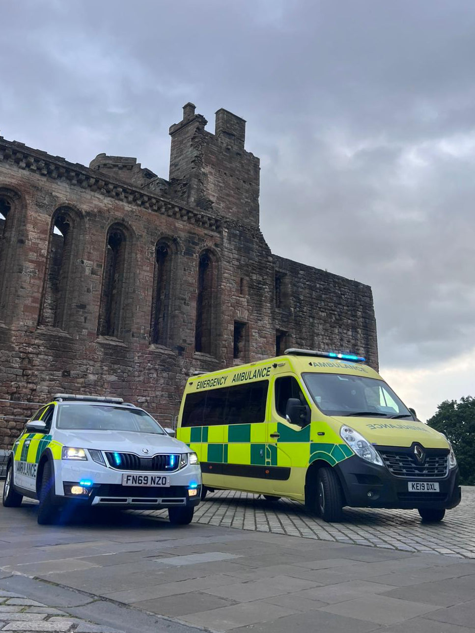 Two emergency vehicles parked in front of a historic building under a cloudy sky.